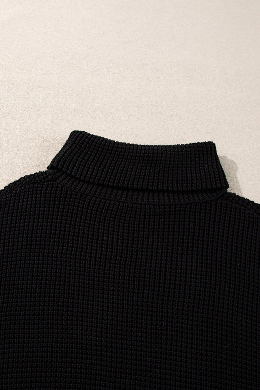 Black acrylic knit turtleneck sweater with ribbed texture and folded collar.