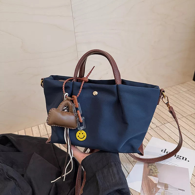 Compact dark blue nylon handbag with brown leather handles and charming smiley face and mini bag charms.