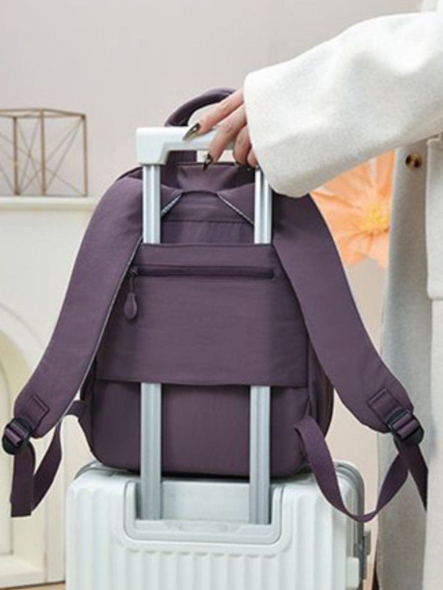 Purple mini Oxford cloth backpack with zippered pocket and adjustable straps on luggage.