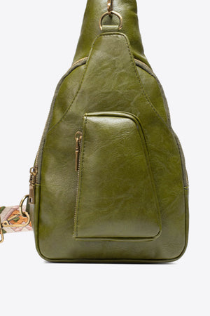 Green textured sling bag with woven strap detail and front zip pocket.