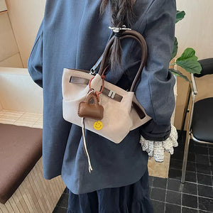 Elegant suede and leather mini tote handbag in light beige with brown trim and a smiley face charm.
