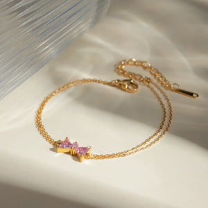 Gold chain bracelet with two pink gemstone bow charms and a lobster clasp.
