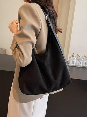 Black suede hobo bag with adjustable strap, worn casually.