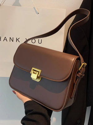 Brown shoulder bag with gold buckle flap detail and adjustable strap.