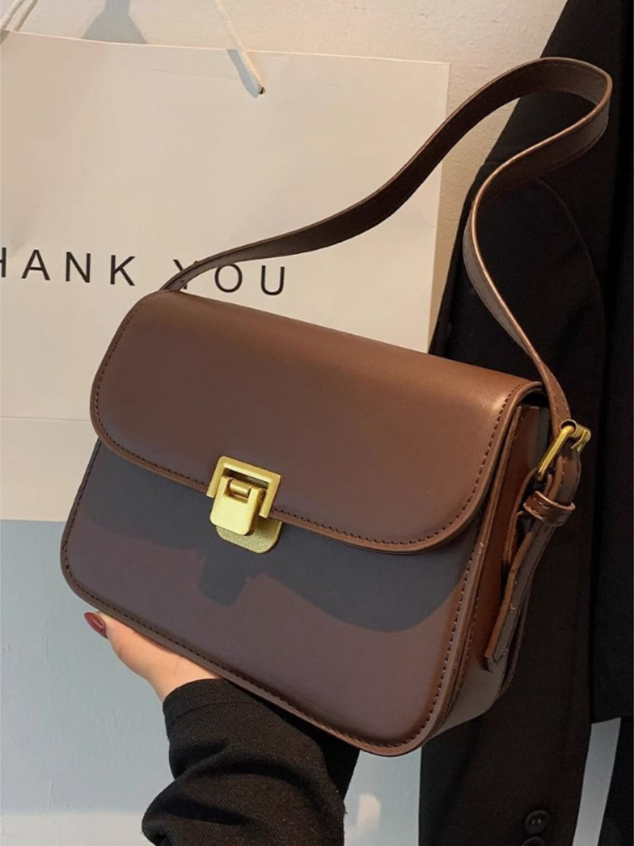 Brown shoulder bag with gold buckle flap detail and adjustable strap.