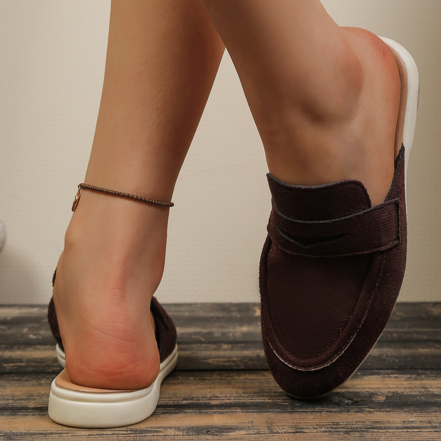 Brown suede backless loafers with round toe and strap detail.