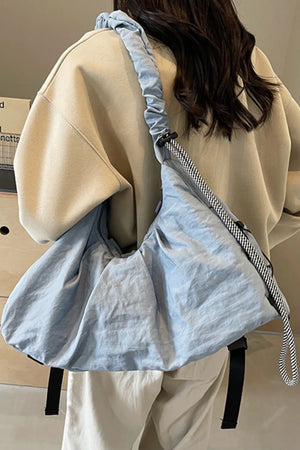 Light blue gathered crescent shoulder bag with ruched strap and black and white rope detail