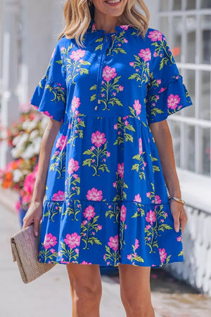 Tiered floral cotton dress with ruffle sleeves and tie neck in blue with pink flowers.