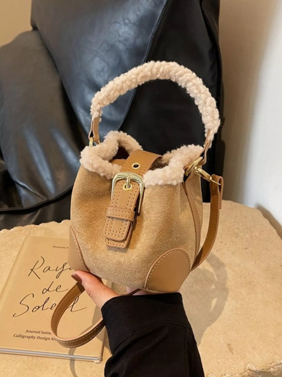 Fuzzy trim crossbody bucket bag in tan suede with leather accents and buckle closure.