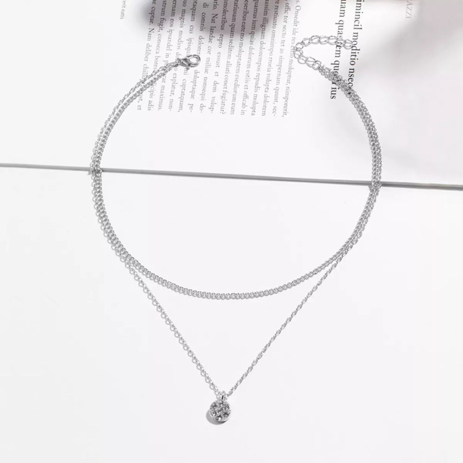 Silver double layered pendant necklace with delicate chains and a small textured pendant.
