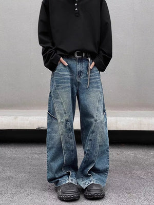 Men's washed wide-leg jeans in blue denim with diagonal seams and distressed details.