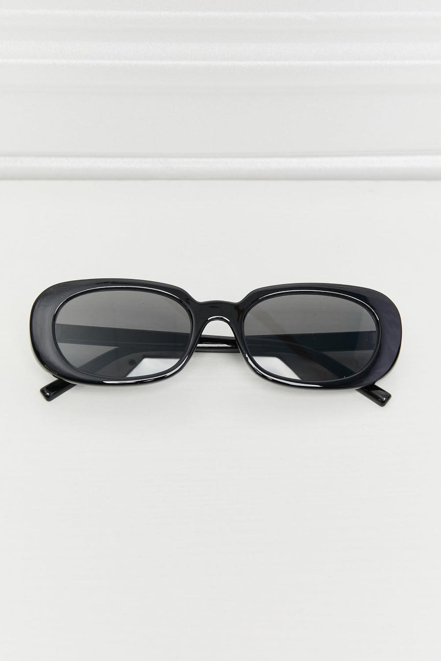 Black oval sunglasses with dark tinted lenses and a glossy finish.