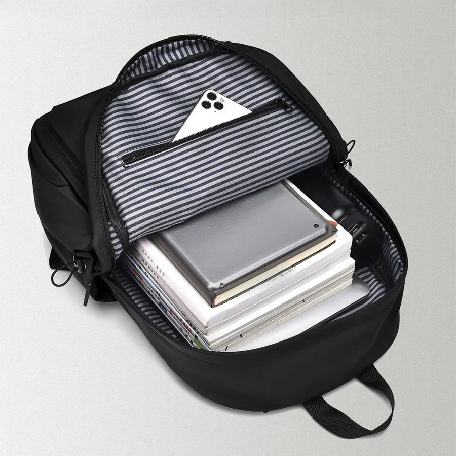 Black commuter backpack interior with striped lining, showing books, tablet, and phone.