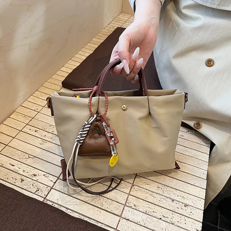 Compact Khaki nylon handbag with brown handles and playful charms.