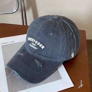 Grey distressed baseball cap with embroidered "EVERYHOUR AND MOMENT" text and side logo.