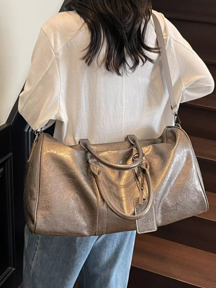 Textured metallic duffle bag in champagne color with detachable strap and handle.