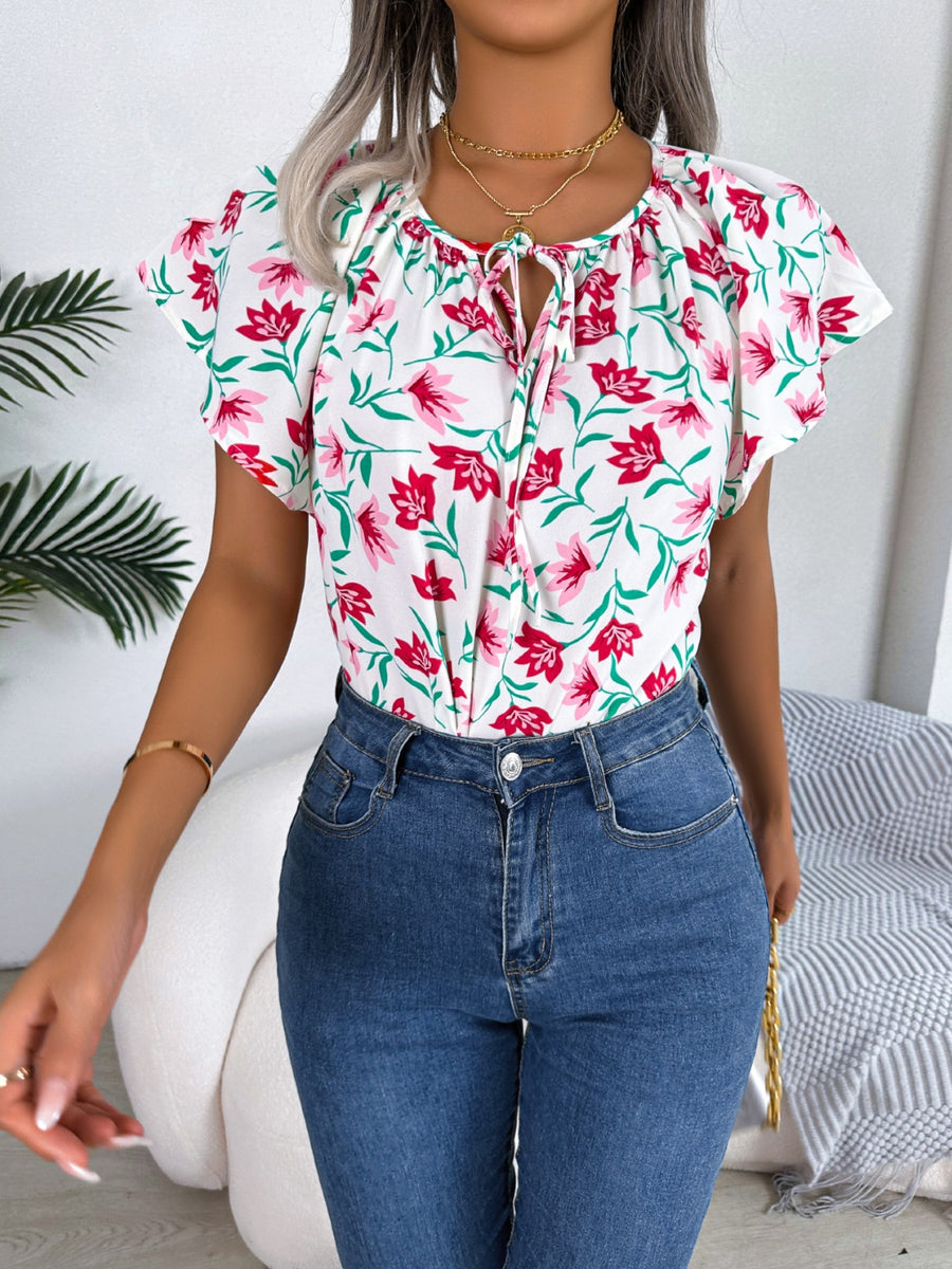 White floral ruffle sleeve tie-neck blouse with pink flowers and green leaves.