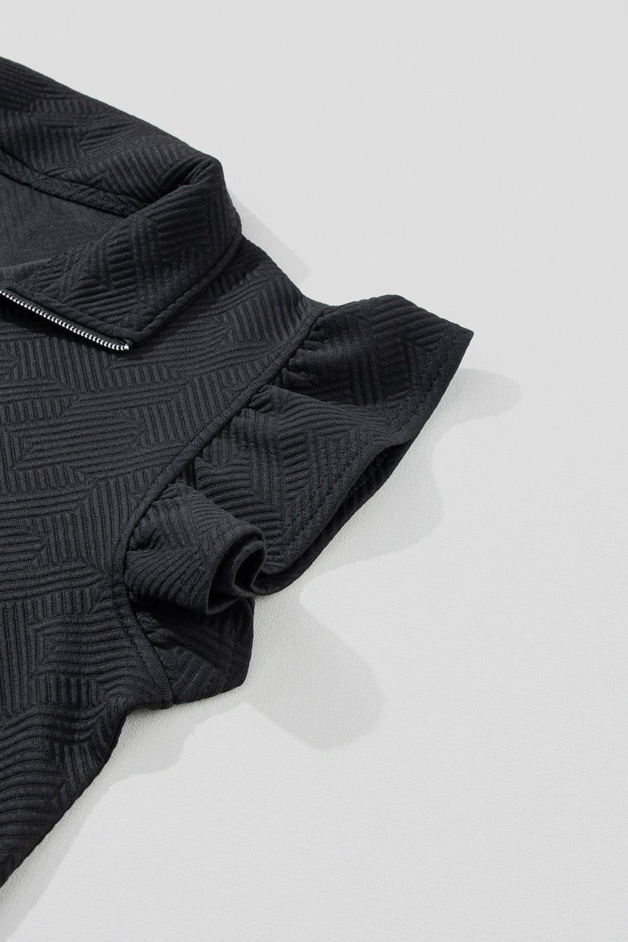 Black zip-up loungewear top with textured geometric pattern and ruffle sleeves