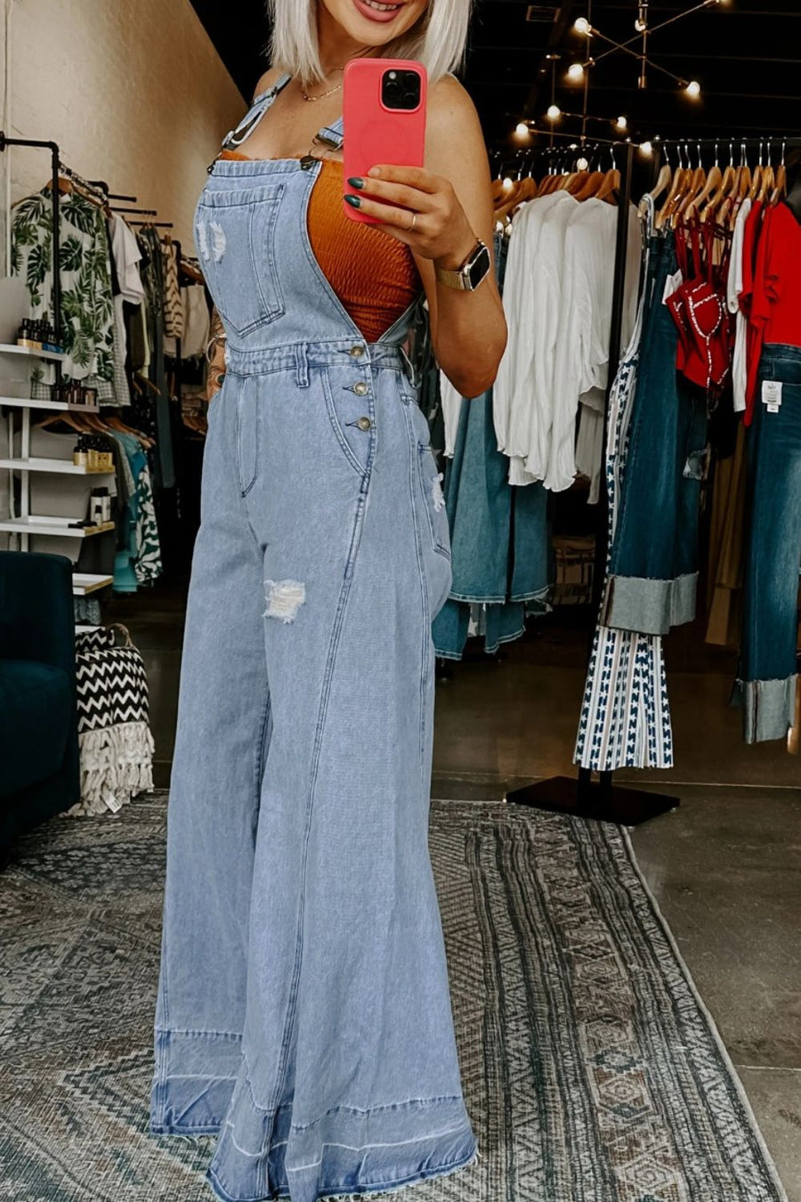 Distressed light wash denim wide-leg overalls with button closures and ripped details.