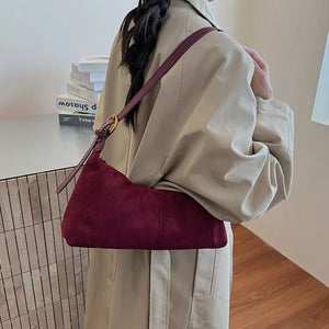 Chic suede crescent shoulder bag in red with adjustable strap and gold buckle detail.