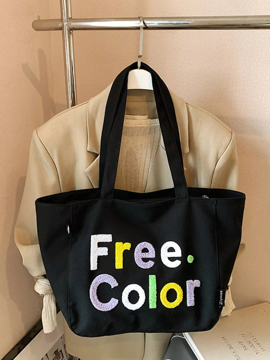 Black canvas shoulder bag with embroidered "Free. Color" text in vibrant letters.