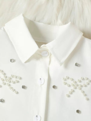 White baby girls' top with pearl bow and rhinestone embellishments.