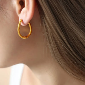 Gold oval hoop earrings with a pearl drop detail, worn by a woman.