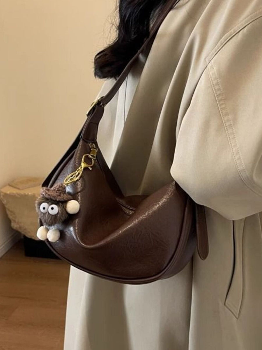 Brown crescent shoulder bag with plush charm and adjustable strap