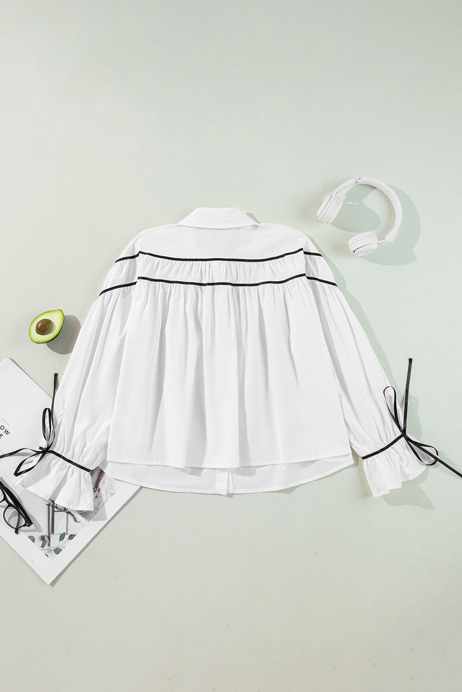 White blouse with black piped trim and bow details on ruffled cuffs.