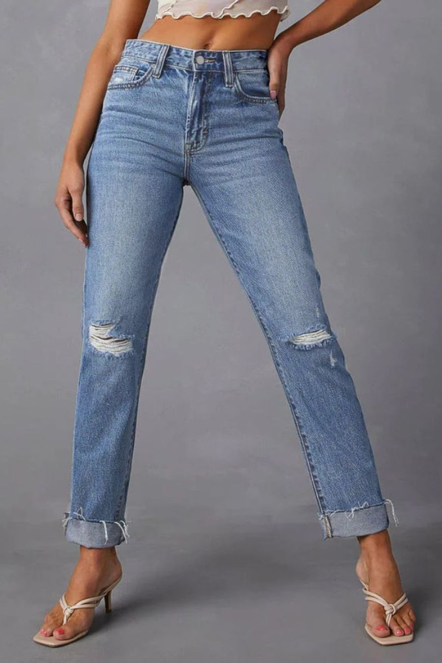 Distressed straight leg jeans in medium wash denim with ripped knees and cuffed hems.