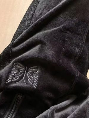 Black velour sweatpants with embroidered butterfly emblem detail.
