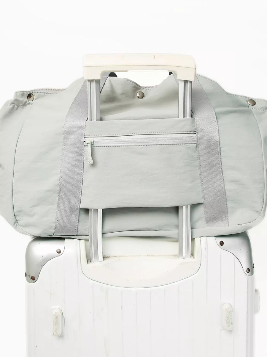 Light gray athletic nylon tote with zippered pocket and trolley sleeve, shown on a suitcase.