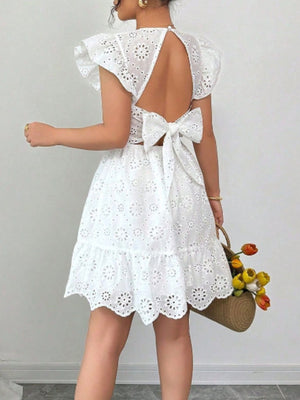 White eyelet mini dress with ruffle sleeves, backless design, and large bow detail.
