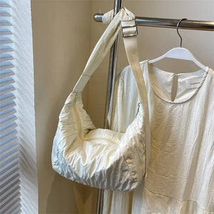 Quilted crescent shoulder bag in beige with adjustable strap and zipper detail.