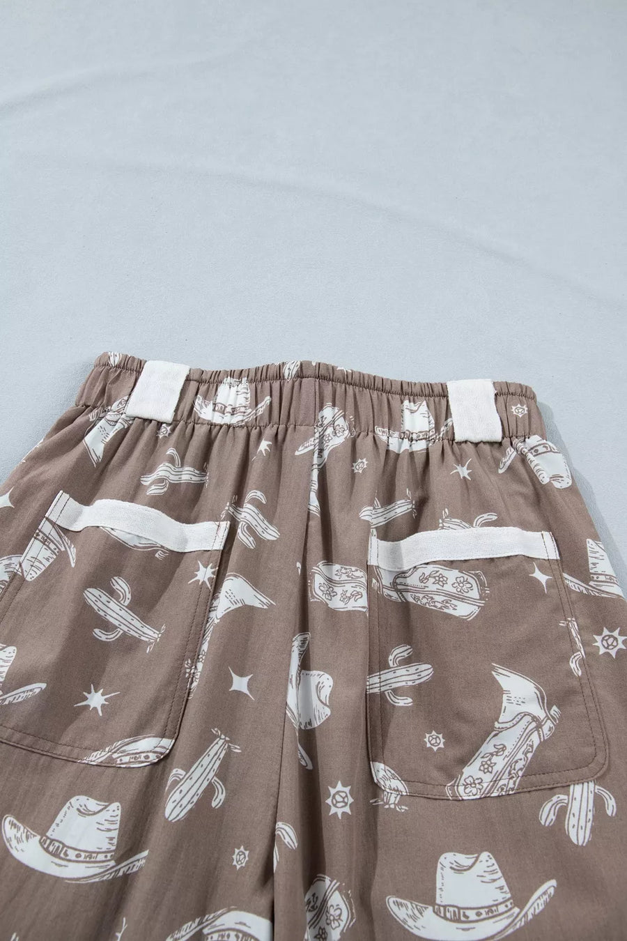 Brown cotton joggers with white western print featuring cactuses and cowboy hats.
