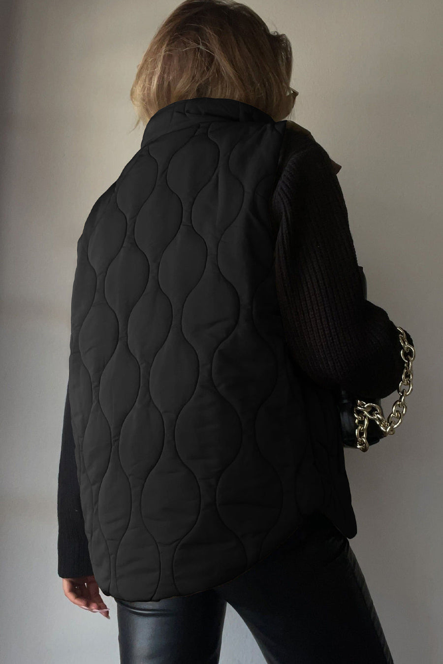 Black quilted stand-collar utility gilet with a wave pattern, worn over a black sweater.