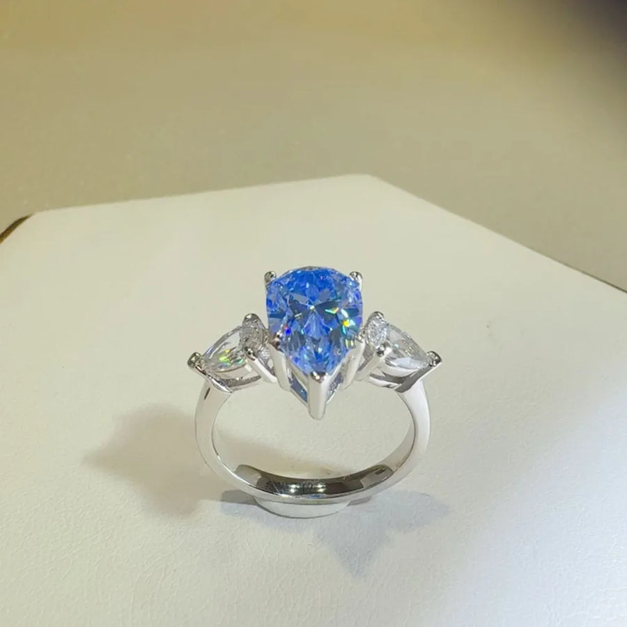 Silver trilogy ring with a large pear cut blue moissanite and two smaller pear cut side stones.