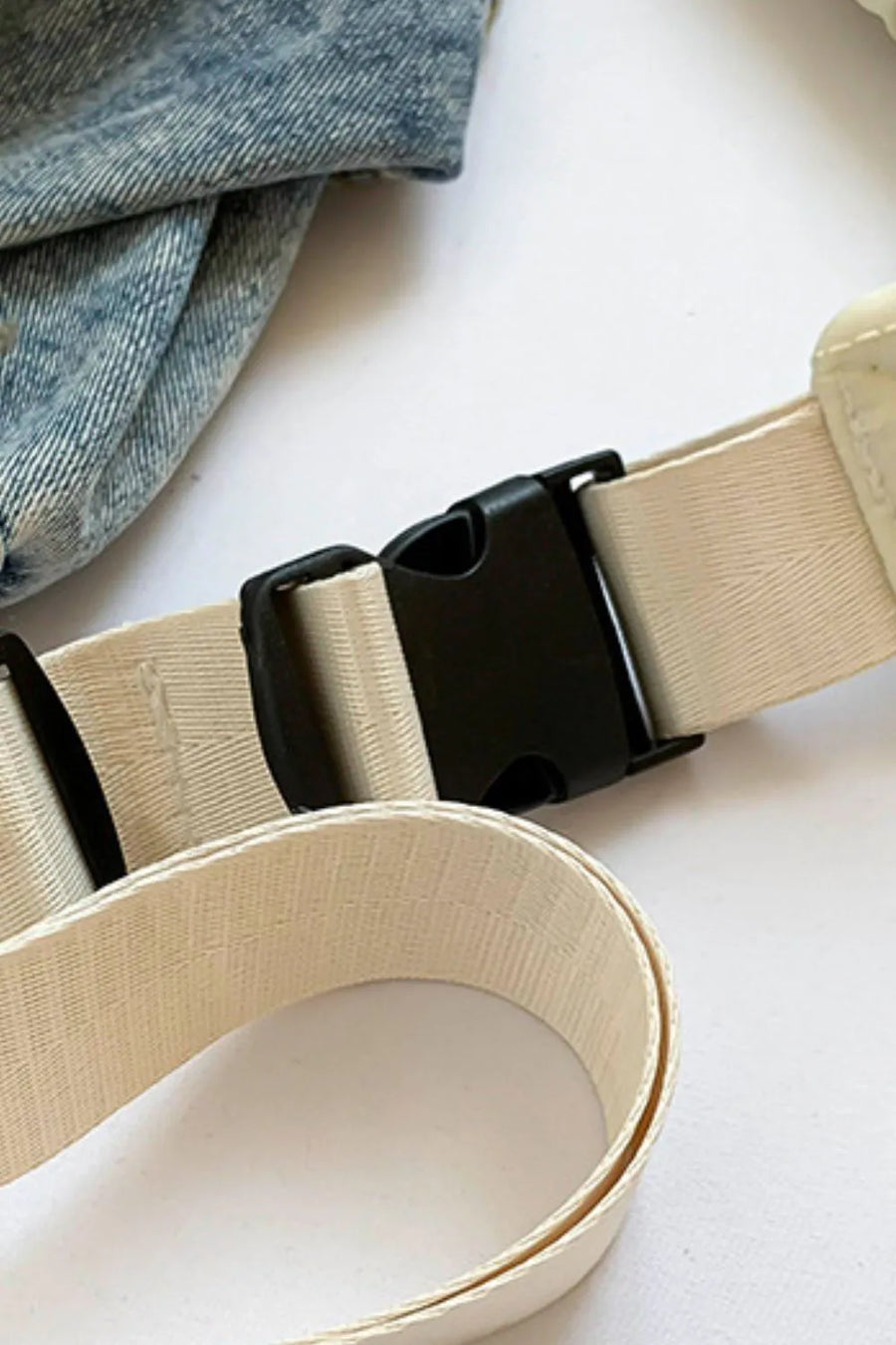 Padded sling bag strap detail with black buckle and ivory webbing.