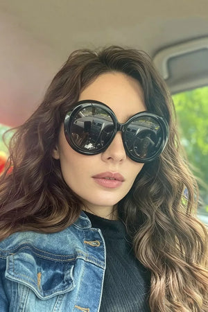 Chic oversized round black fashion sunglasses with bold frames, worn by a woman in a denim jacket.