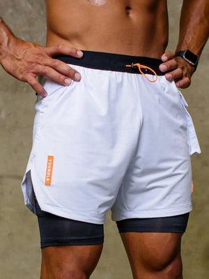 White layered cargo shorts with black compression shorts, orange drawstring, and logo detail.