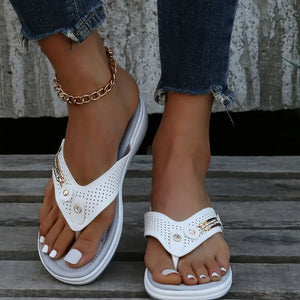 White perforated thong wedge sandals with embellishments and a gold ankle bracelet.