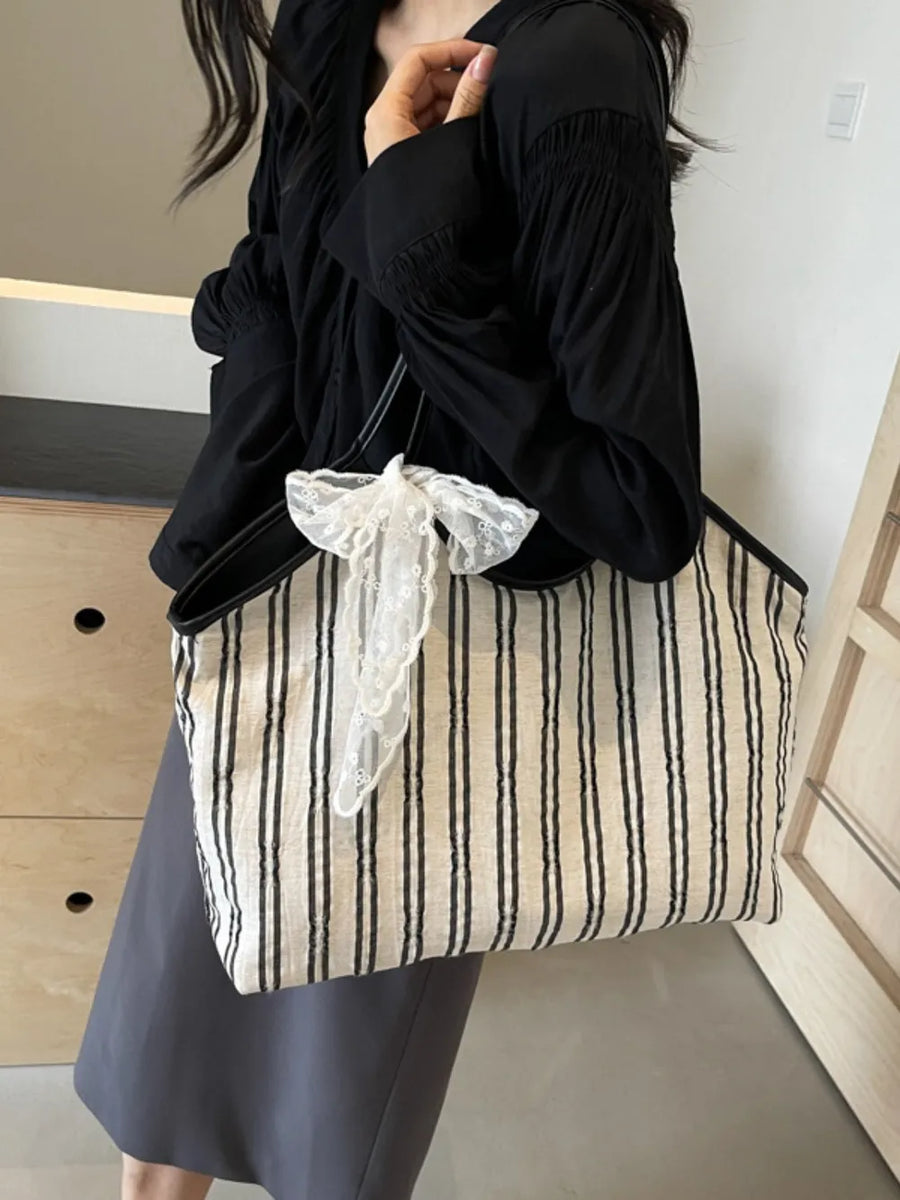 Beige shopper bag with black stripes and a white lace bow detail.