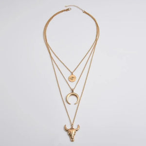 Gold layered pendant necklace with bull skull, crescent moon, and evil eye charms.
