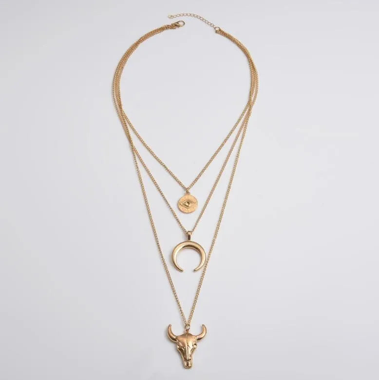 Gold layered pendant necklace with bull skull, crescent moon, and evil eye charms.