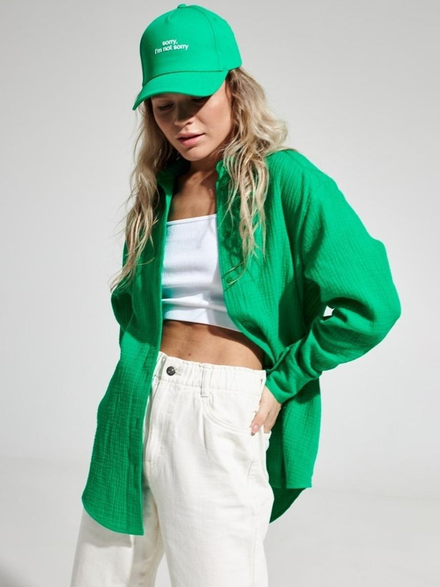 Green textured cotton overshirt with relaxed fit and button front, styled with white tank top and cream pants.