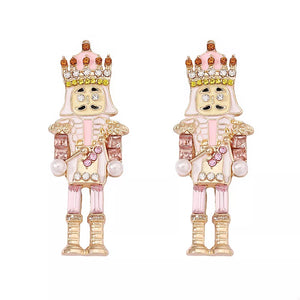 Blush pink nutcracker dangle earrings with crown and pearl details.