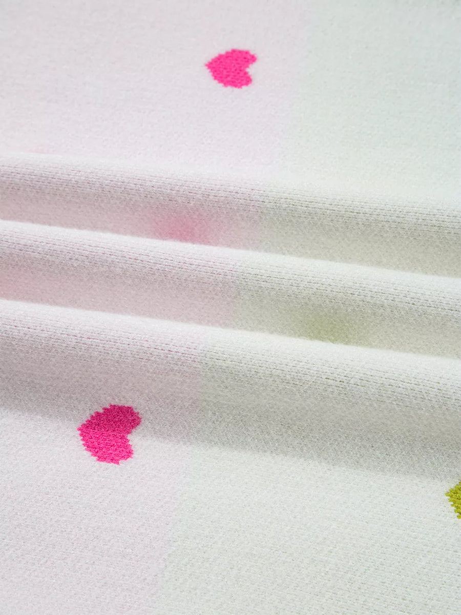 White knit sweater with playful pink and green heart pattern.