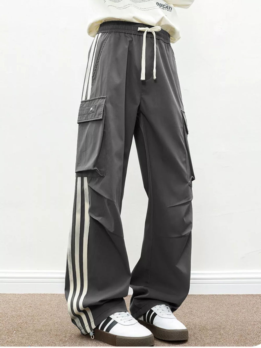 Oversized dark gray cargo pants with white side stripes and flap pockets.
