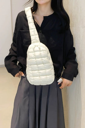 Padded sling bag with top handle in Ivory, featuring a quilted pattern and adjustable strap.