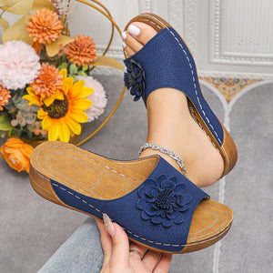 Perforated floral wedge slides in Peacock Blue with white stitching and a brown sole.